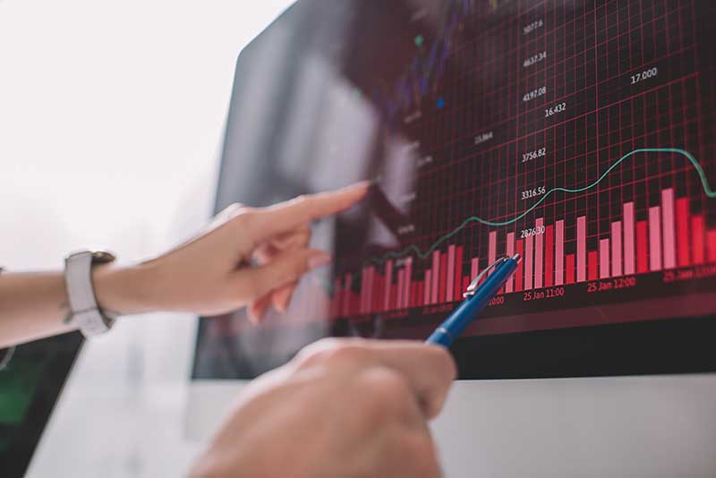 data analytics for business - Hands pointing at and analyzing a financial graph on a computer screen with red bar graphs and a line chart.