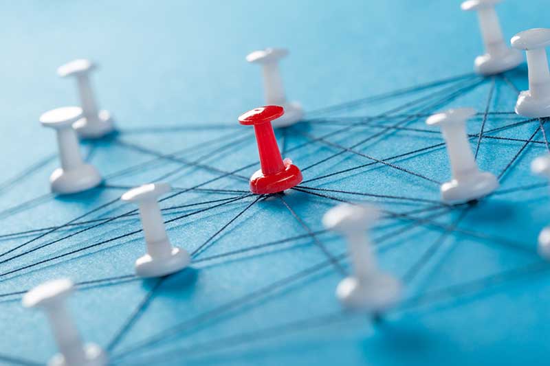 A red pushpin connected with multiple white pushpins by a web of strings on a blue background.