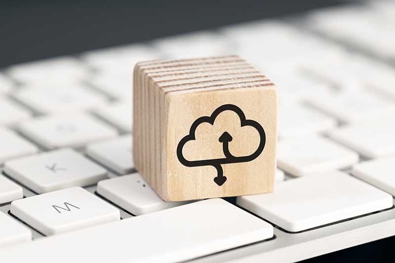 Wooden block with a cloud upload/download icon on a white keyboard.