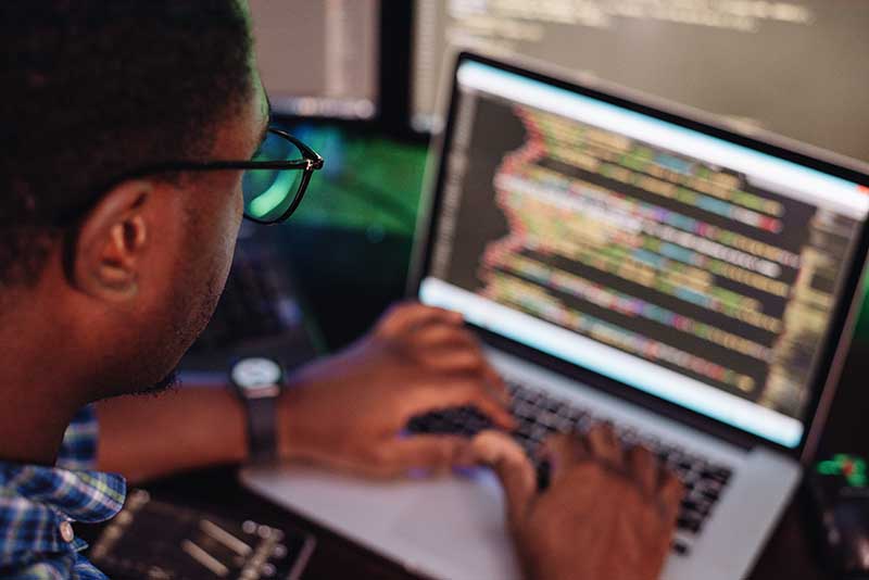 A person is working on a laptop with multiple screens displaying lines of code.