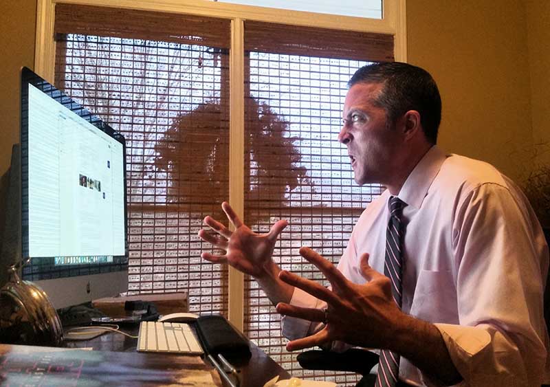 Man in business attire gesturing angrily at a computer screen.