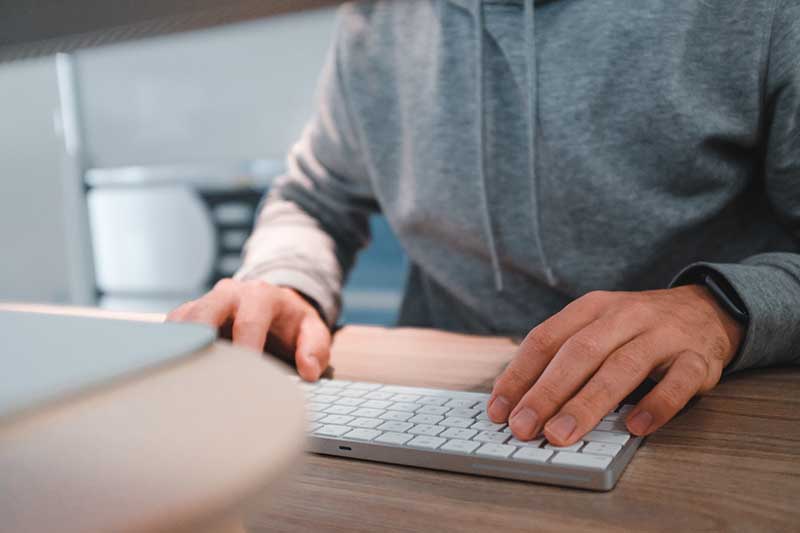 greater boston IT services - Person typing on a keyboard, wearing a grey hoodie.