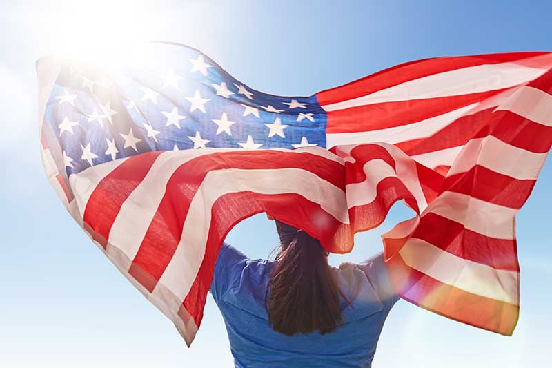 Man holding an American flag against a sunny sky.