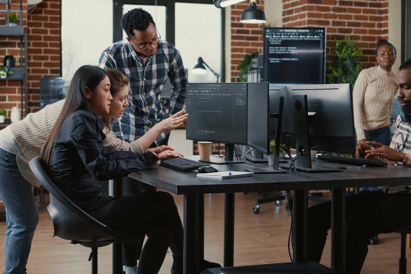 Group of people working together in a modern office, focused on computer screens displaying code.