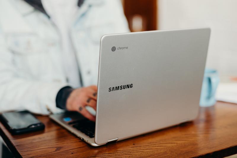 Person using a Samsung Chromebook, typing on a keyboard at a wooden desk.