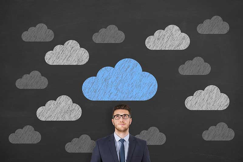 Man in suit with blue cloud drawing overhead, surrounded by grey clouds on a blackboard.​